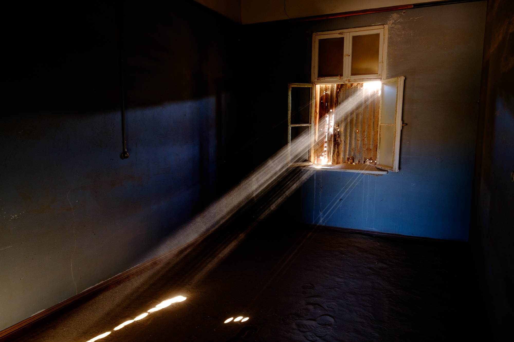 Light beams through rusted iron boarding up the window of this room in the school